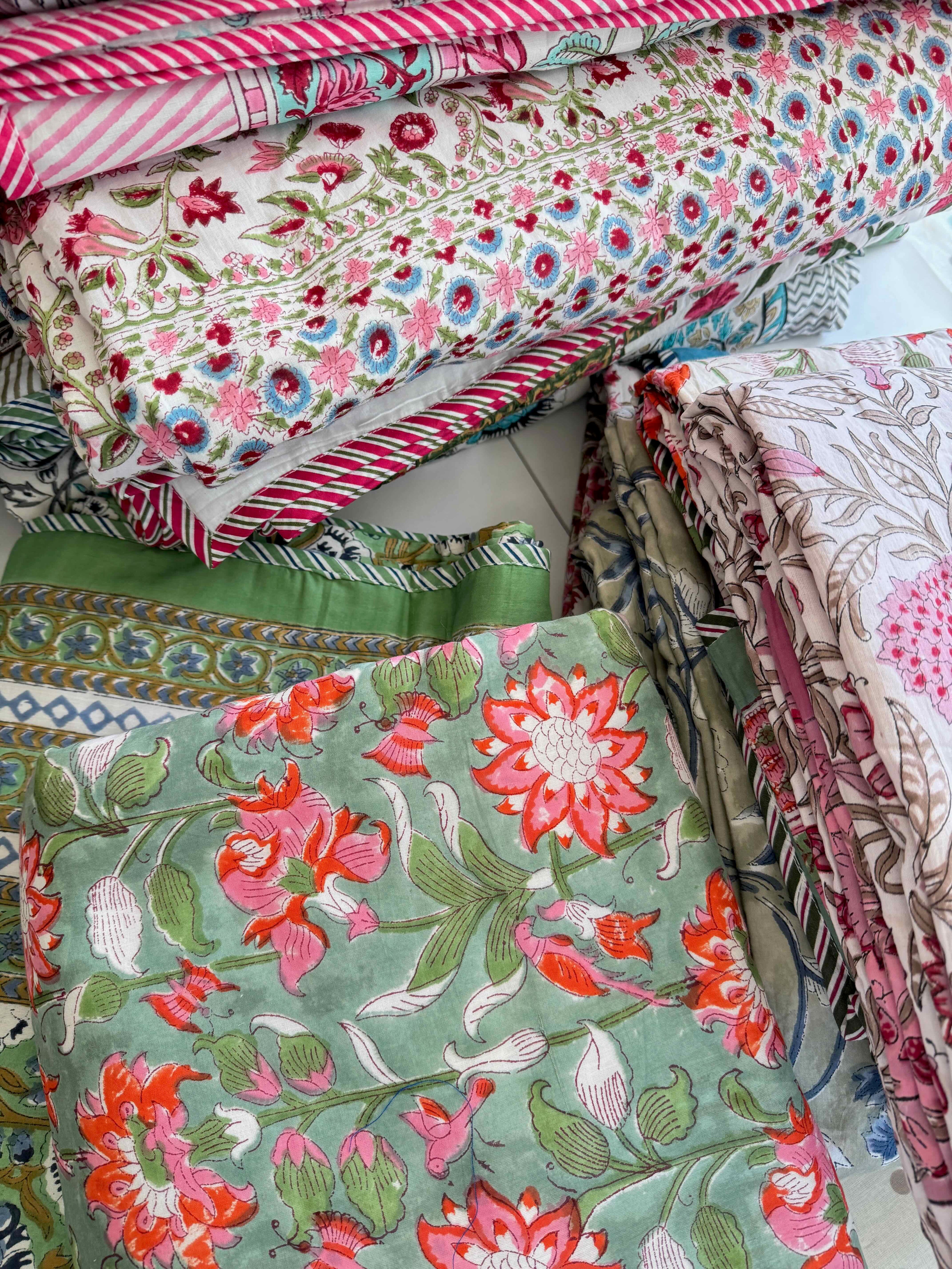 Stack of colourful bed throws with floral and patterned designs.