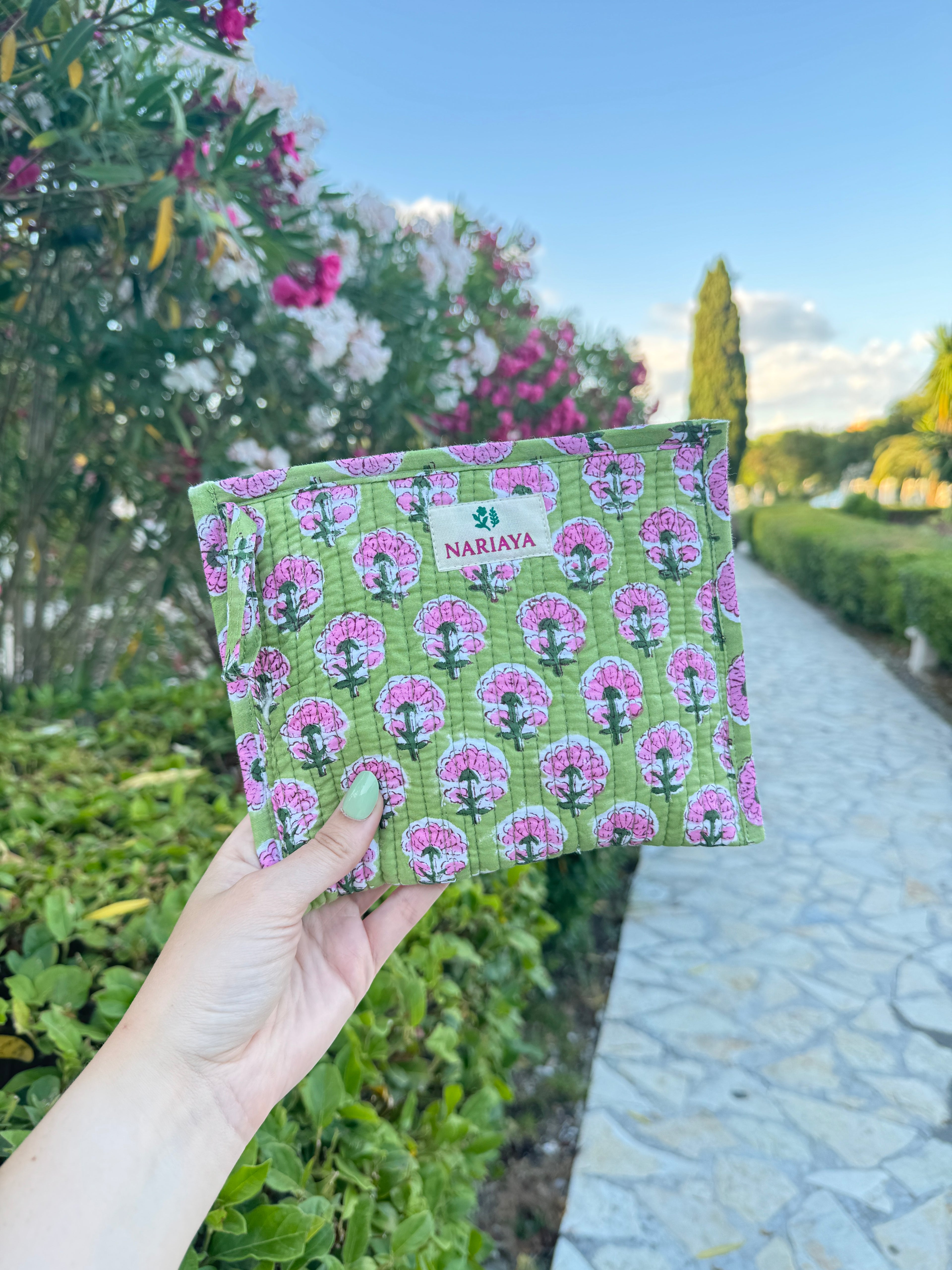 Hand holding a green and pink patterned product with flowers and plants in the background