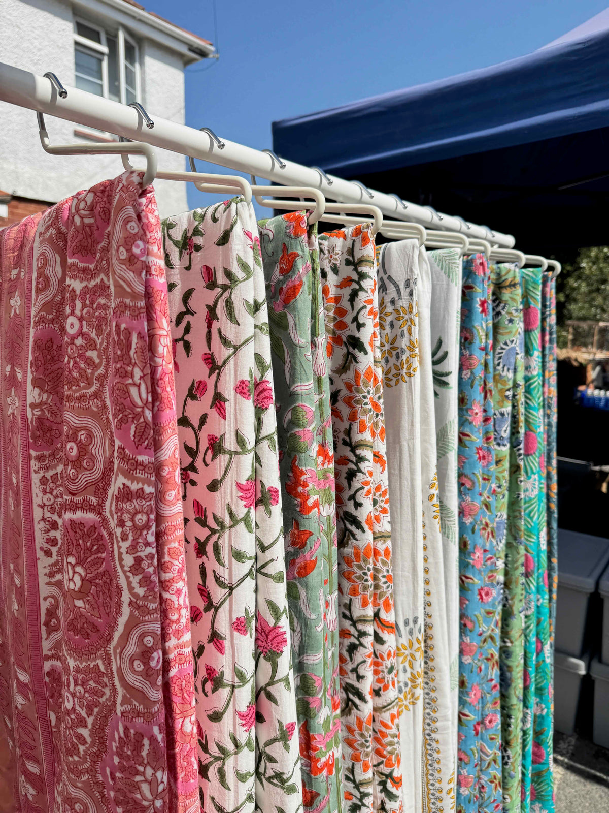 Colorful patterned bed throws hanging on a rack outdoors.
