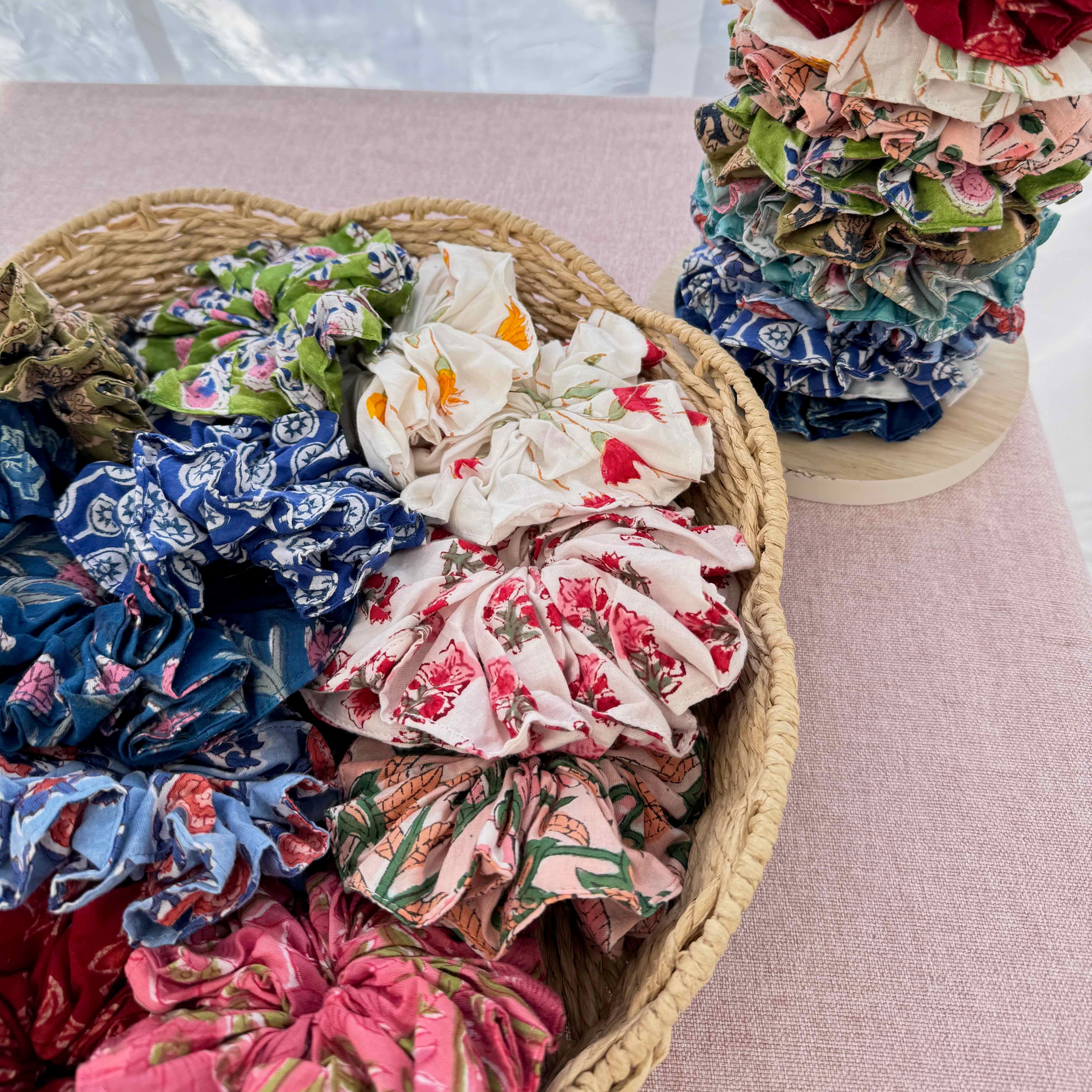 Basket of colorful floral scrunchies on a pink surface with a white curtain background